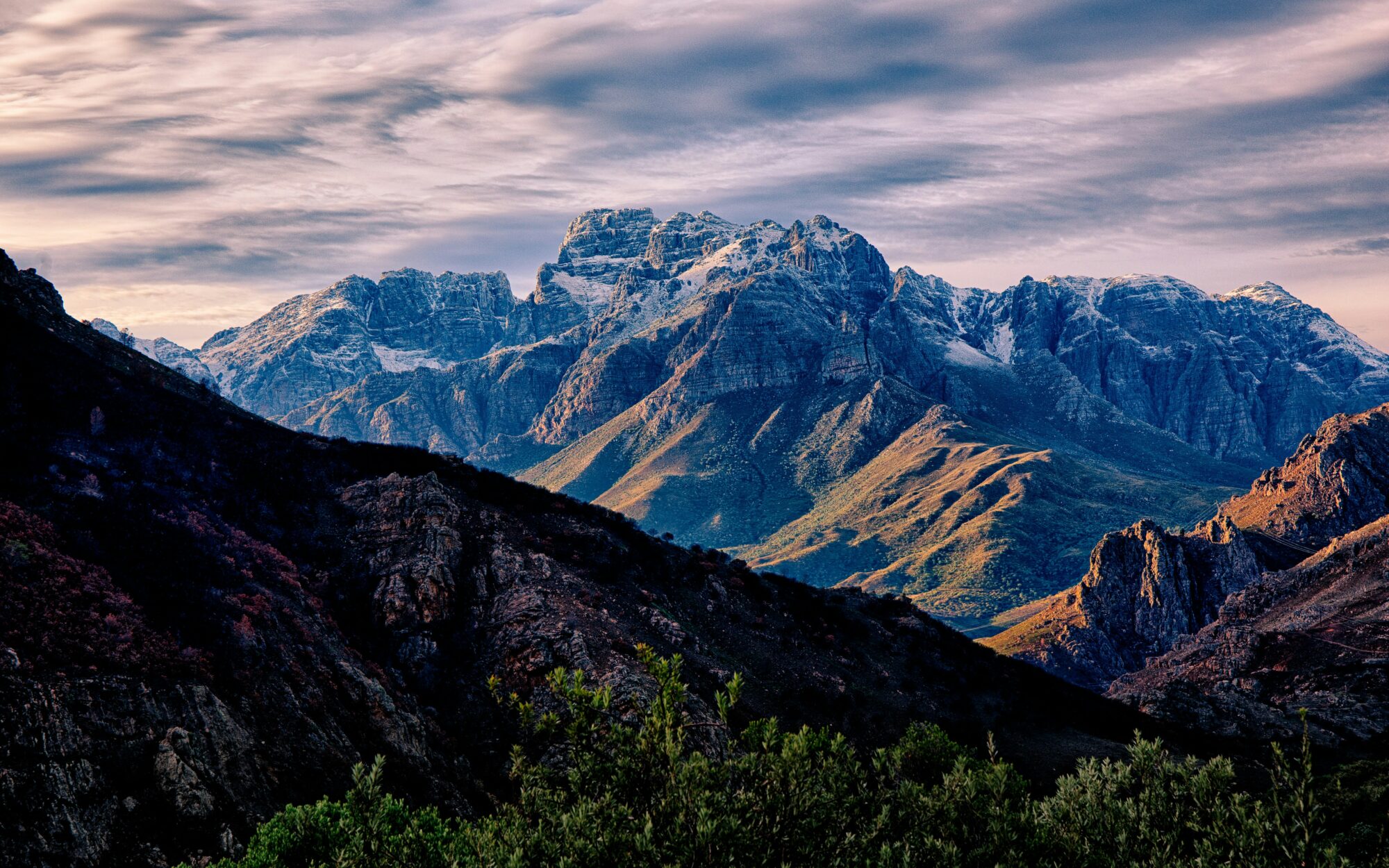 Mountain range under a cloudy sky at sunset.