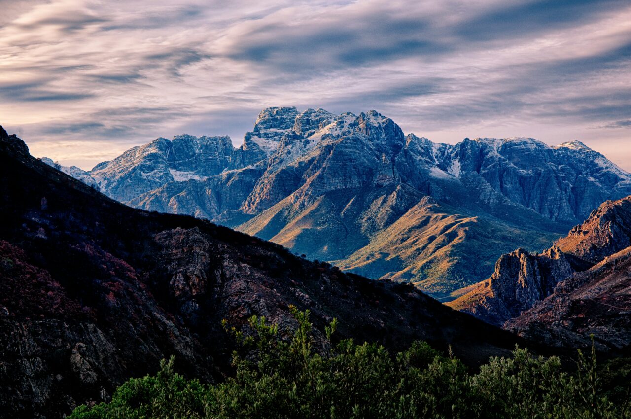 Majestic mountain range with rugged peaks and shadowed valleys under a cloudy sky.